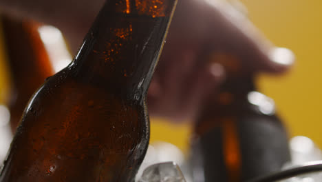 Nahaufnahme-Einer-Person,-Die-Eine-Gekühlte-Glasflasche-Kaltes-Bier-Oder-Alkoholfreie-Getränke-Aus-Einem-Mit-Eis-Gefüllten-Eimer-Vor-Gelbem-Hintergrund-Nimmt-1